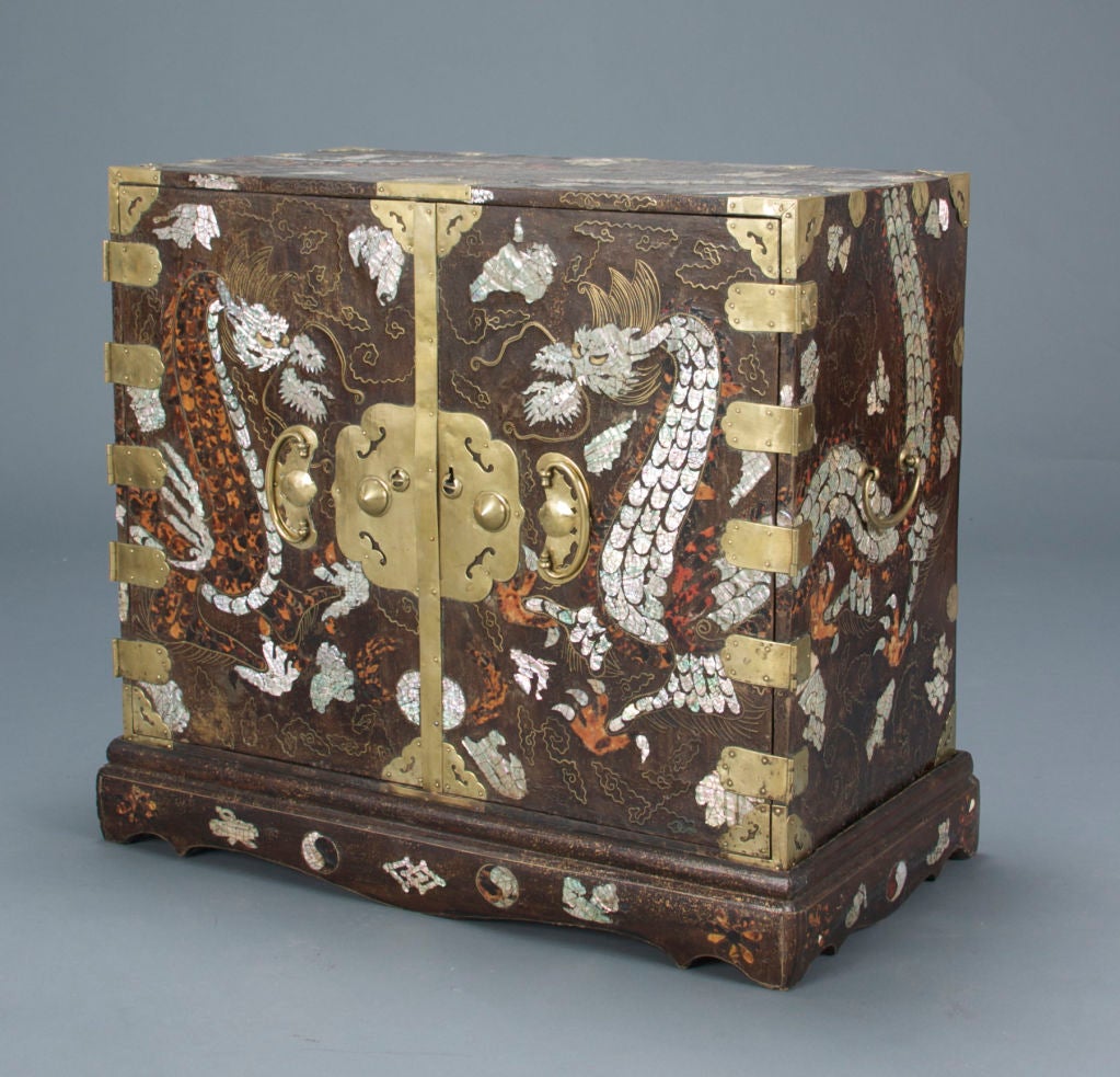 Decorated with serpentine confronting dragons over the flaming pearl, with tossing mane and whiskers, the bodies continuing on to the sides and top of the chest, the cartouche form escutcheon flanked by bat shaped handles, opening to six drawers,