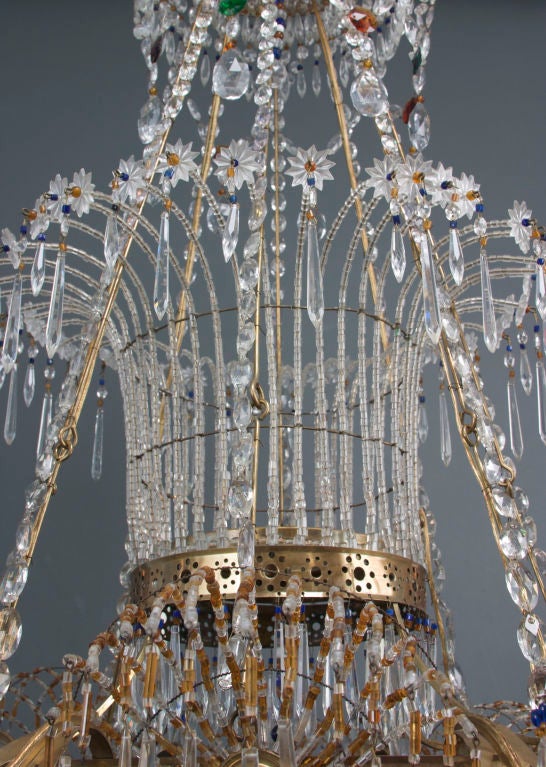 This large-scale, magnificent chandelier with colored and clear crystals is mounted with a circular banded corona issuing sprays of flower heads and hung with glass pendant swags. The next pierced brass tier suggests a water fountain, decorated with