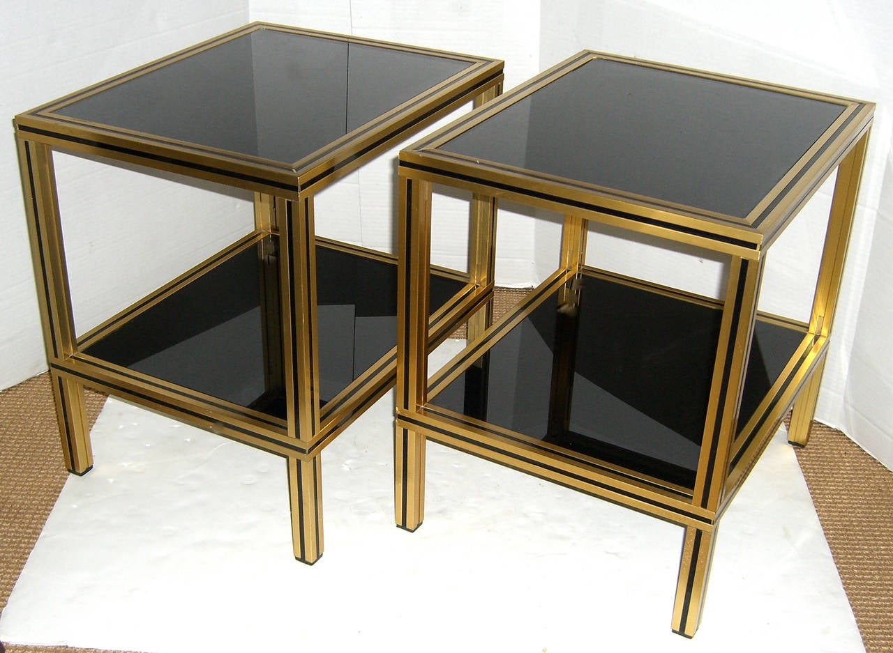 A pair of 1970s French modernist end or side tables. Gilt brass is accented with inset black detail, shelves are drop in opaque black glass.