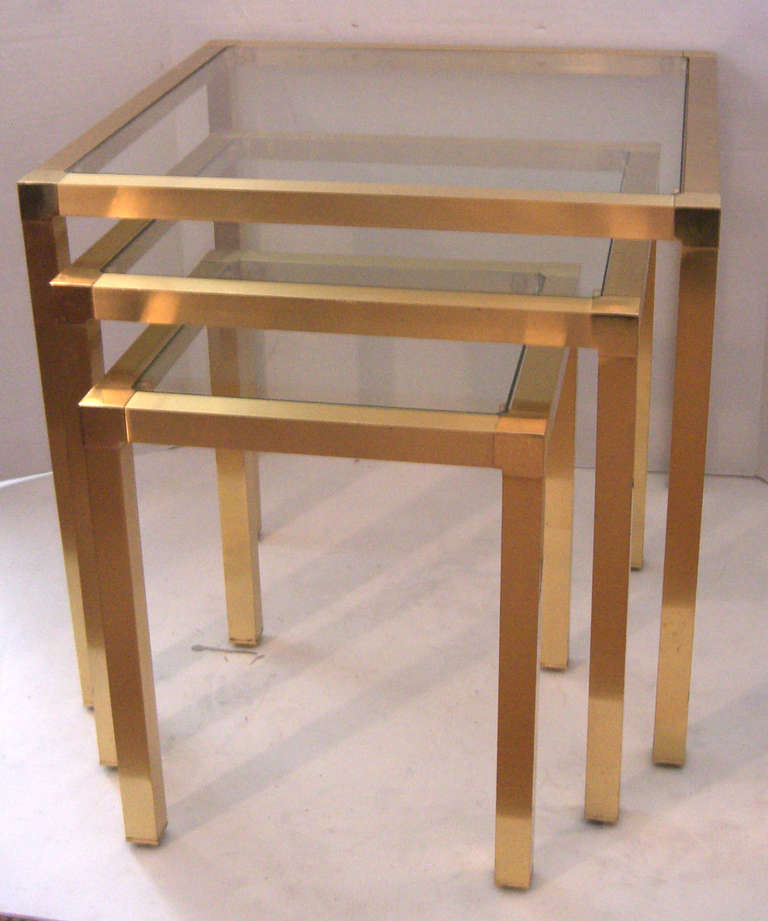A set of 3 modern design nesting tables in a bright gold finish. Each table has a clear glass inset top.
