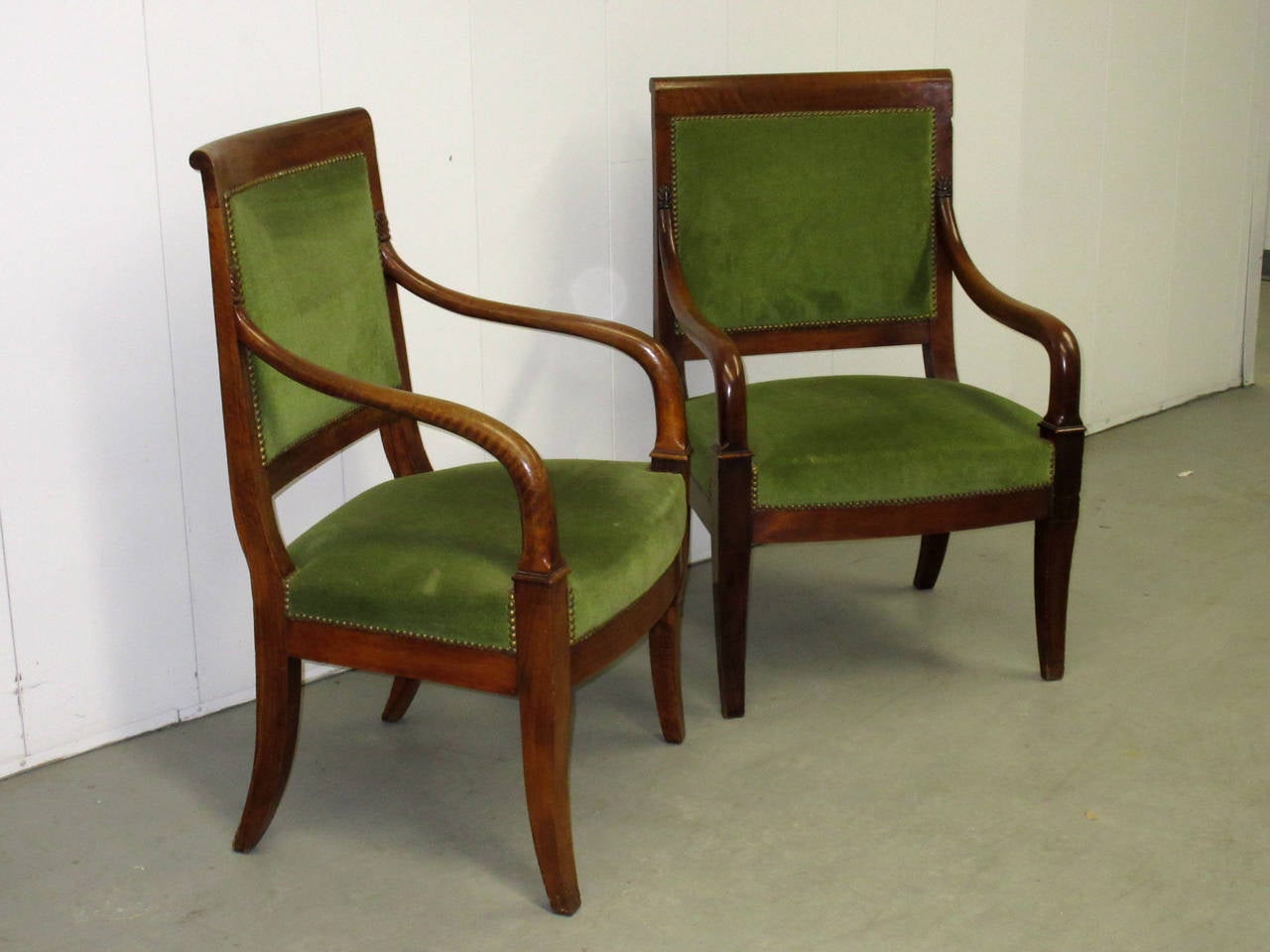 Early 19th Century armchairs of identical design. One chair is narrower with higher arms. Both are upholstered in green velvet and finished with brass nailheads.