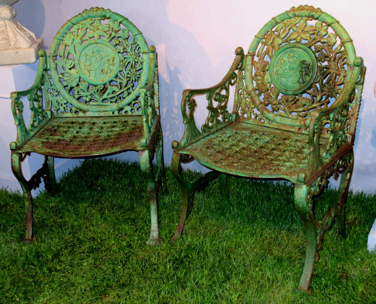 A pair of cast iron garden armchairs with a unique and detailed Indonesian design. The center medallion depicts three figures, and is surrounded by a tropical floral design. Each arm is adorned with a stylized monkey figure.