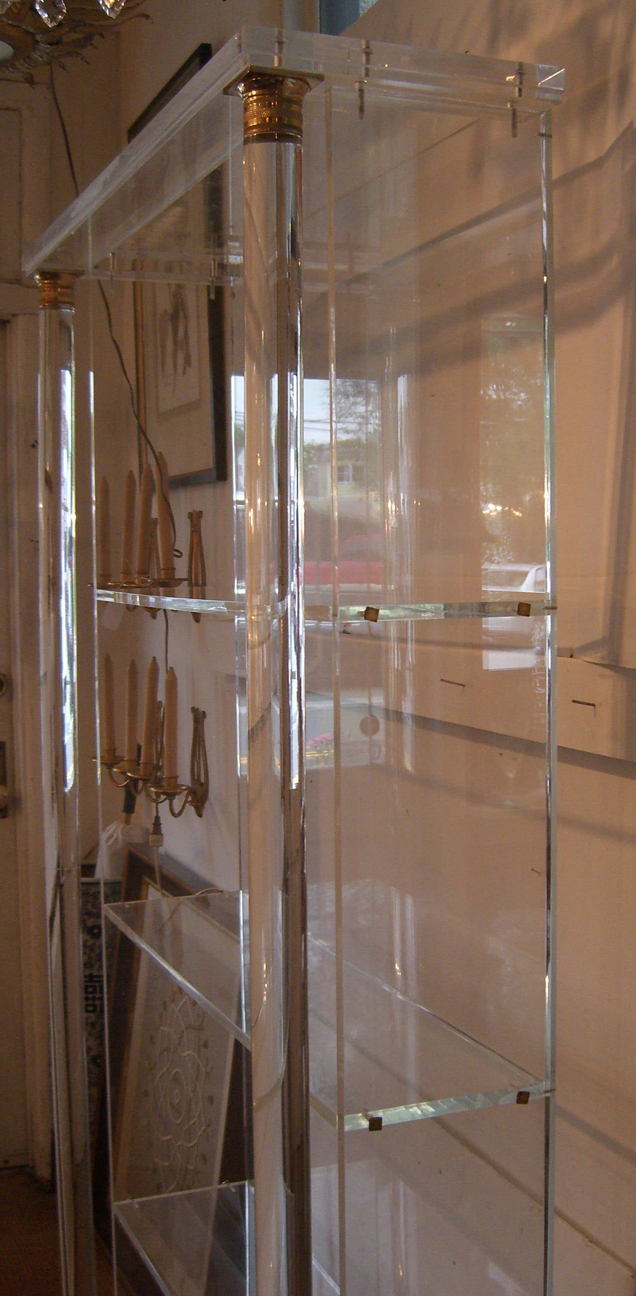 A tall solid clear Lucite bookshelf with columns and brass accents. Three thick Lucite shelves are help with brass screws and can be removed.