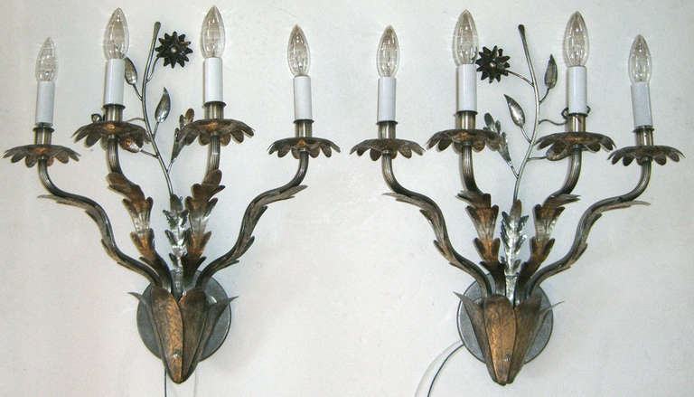 A pair of four-arm nickel-plated brass wall sconces. A simple design is hammered into the metal and a long stem with leaves and flower stands behind.