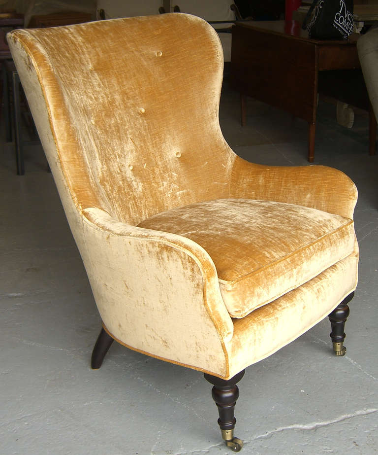 Four wingback armchairs upholstered in a soft yellow velvet with button-tufted backs,  and turned front legs fitted with casters