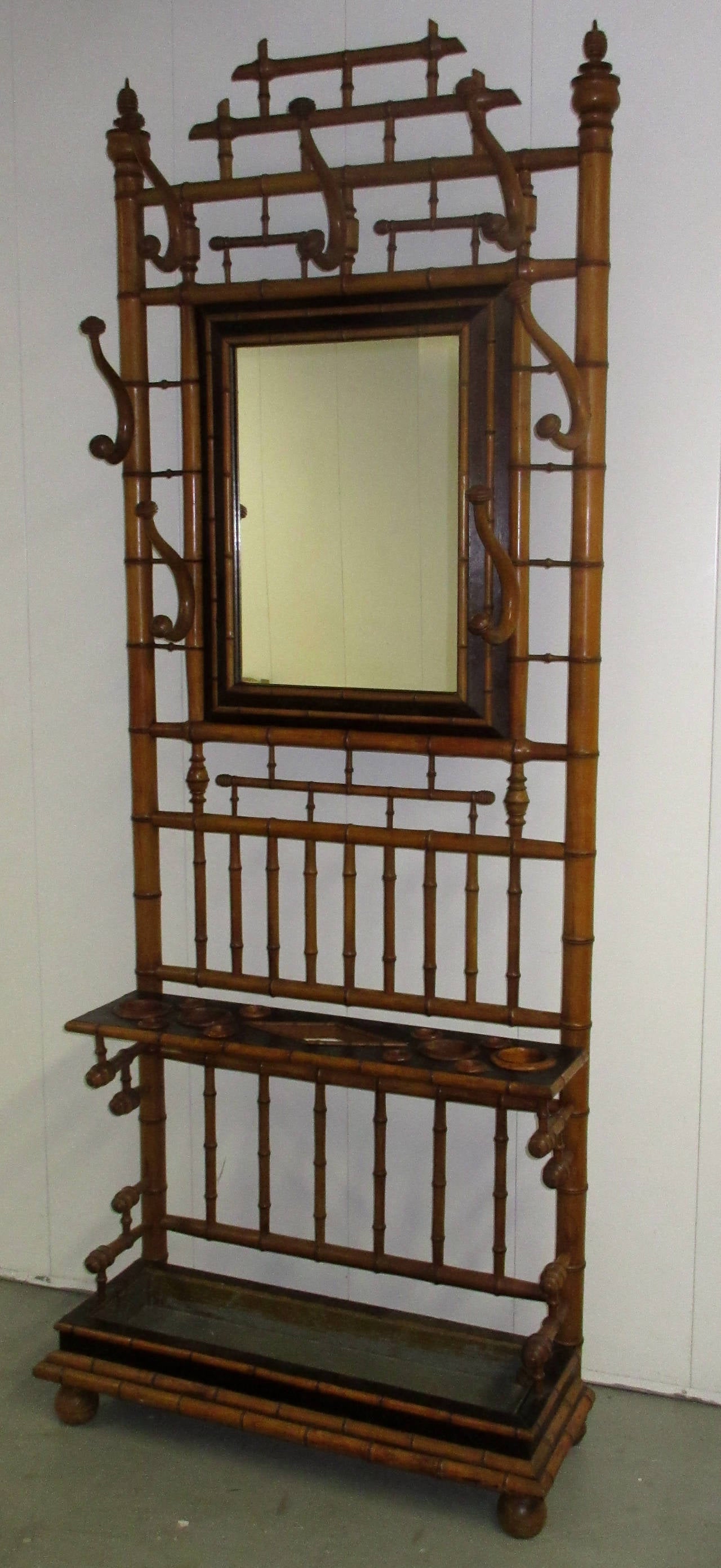 An early 20th century French bamboo hall Stand with framed mirror. The piece stands on call feet and is topped with turned finials. There are seven scrolled hangers and a slotted shelf with a tin insert below.