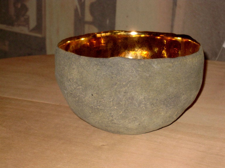 This vessel was created by Cristina Salusti. Beginning with a ball of clay, she pinches it into vessels and textures them with stone fragments. After multiple firing it was finally lustered  22K gold . Its volcanic-like outer wall seem almost