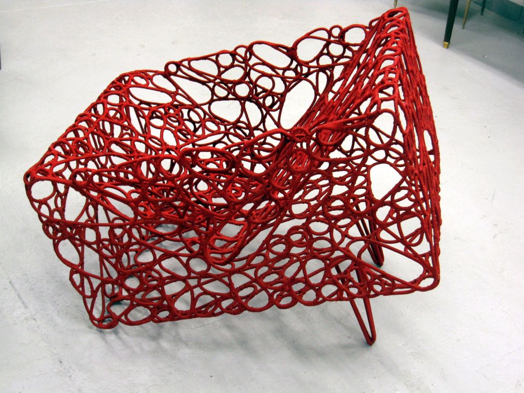 An architectural chair with a solid square form given the appearance of lightness by dozens of cut pieces of metal assembled by hand and woven in nylon fishing nets. The chair is the work of a French artist born in Mali who was inspired by