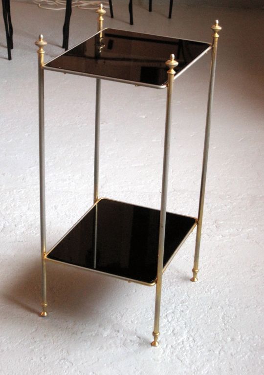 An elegant pair of side tables in gold metal with two black glass shelves. Classic legs and finials.