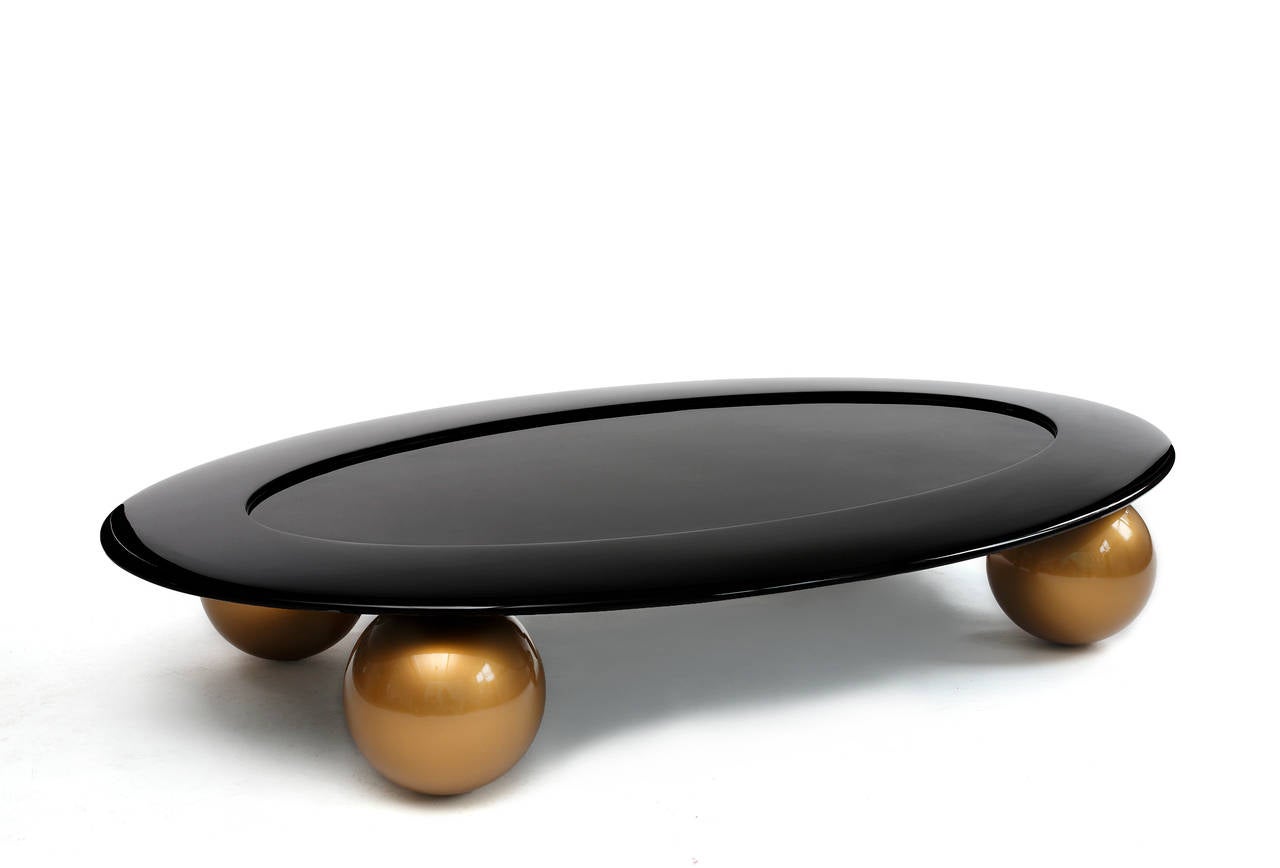 Ein atemberaubend eleganter Cocktailtisch von Tinatin Kilaberidze mit einer ovalen Platte aus schwarz lackiertem Holz, die auf großen, goldlackierten Kugeln sitzt.
Exquisite Proportionen.