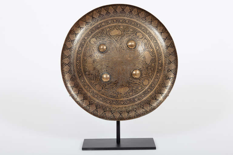 This fine Indian or Persian small-sized Dhal shield is circular in form, all finely decorated with damascened ornament of stylized foliate motifs, with four raised bosses on the front, securing four leather straps on the back, all now raised on a