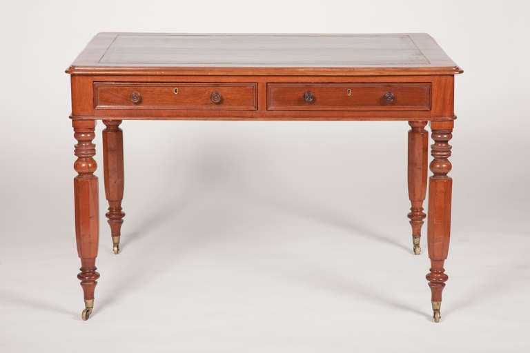 This English William IV period mahogany writing table has an inset green leather writing surface with parcel gilded tooling, above two drawers, raised on four turned legs, ending in brass casters.