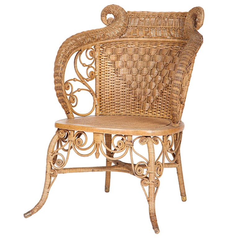 This late nineteenth century American wicker and cane slipper chair, attributed to Heywood-Wakefield, has an intricately caned and spindled back, scrolling shaped arms, supported by out swept legs, joined by a cross stretcher, with scrolling