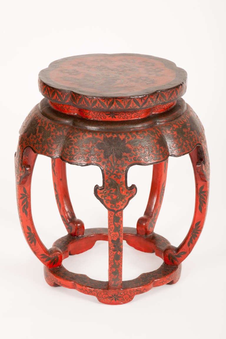 This Chinese Qing Dynasty lacquered drum stool, or low table, has incised and polychrome decoration of exotic floral and foliate motifs on a red lacquered ground on the cinquefoil top, the shaped apron, the five curving legs and the bottom