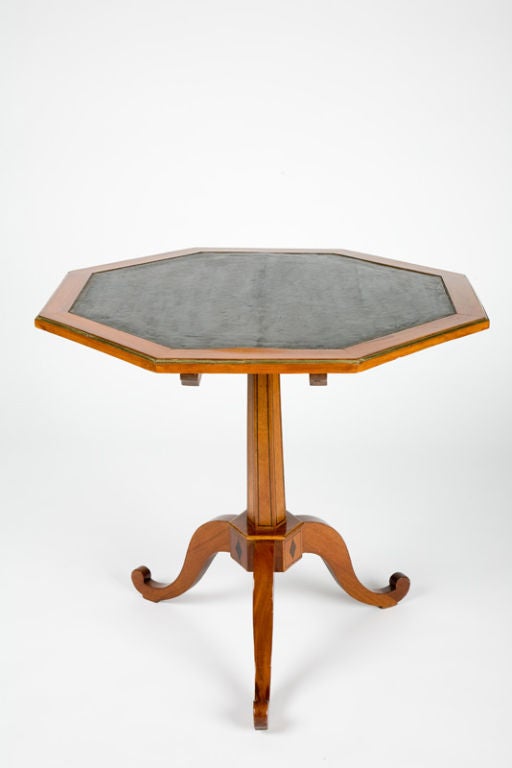 This French Directoire period tripod table or gueridon, has a tilting octagonal top with an inset black leather surface with gilded tooling and edged with a bronze molding. The curved fruitwood legs are joined by a hexagonal block, decorated with