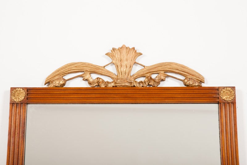 This Italian neoclassical style mirror has a walnut frame with fluted moldings, punctuated at the four corners with gilded wooden rosettes, the top with a gilded wooden cresting of stylized wheat sheaths, all raised on gilded wooden cornucopia feet,