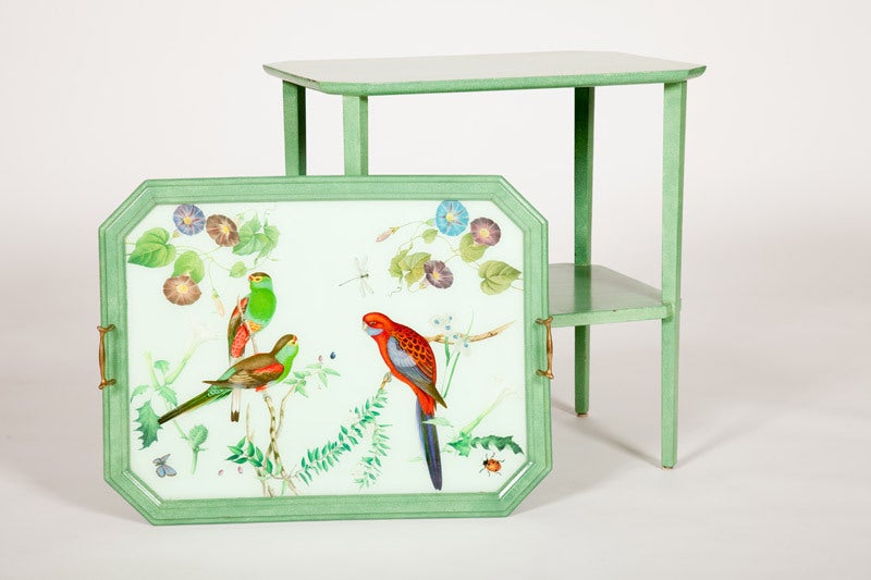 This mid-20th century American table, with canted corners, one shelf and a removable tray top, is painted a mottled green. The tray top has two brass handles and an inset decoupage decorated glass top with nineteenth century colored engraving