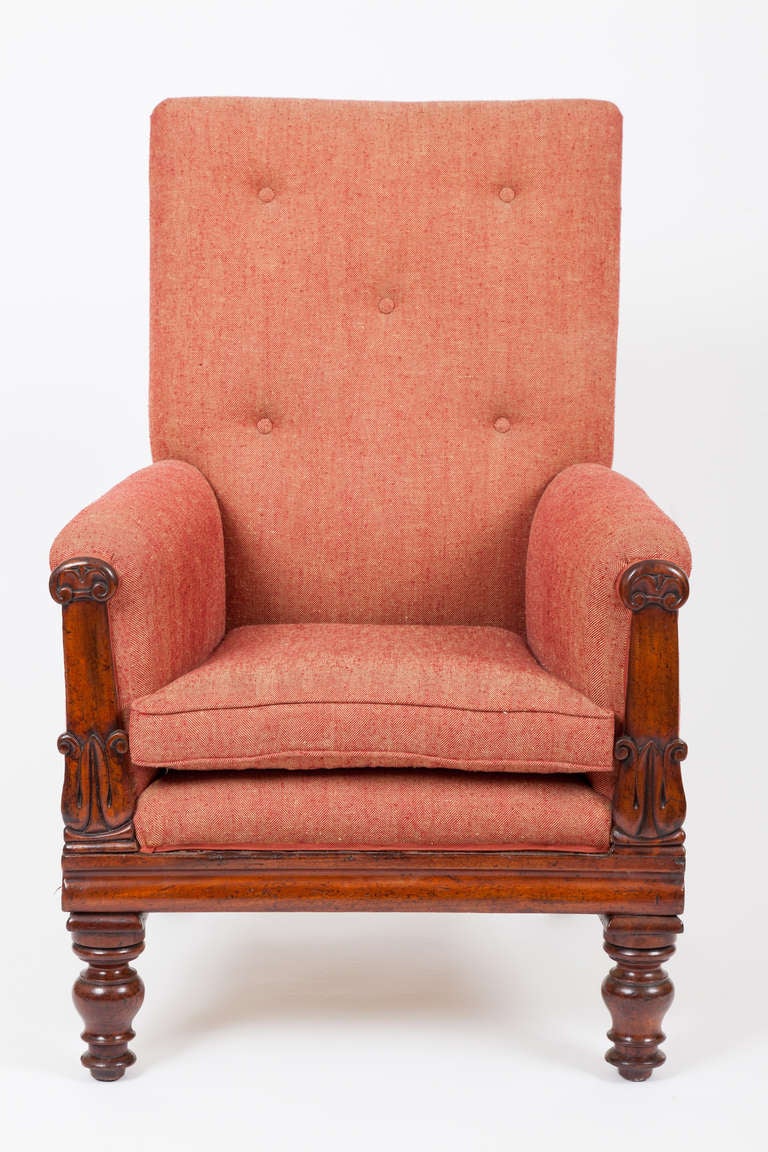 This English William IV period mahogany armchair has an upholstered back and seat with carved arm decoration raised on turned legs.