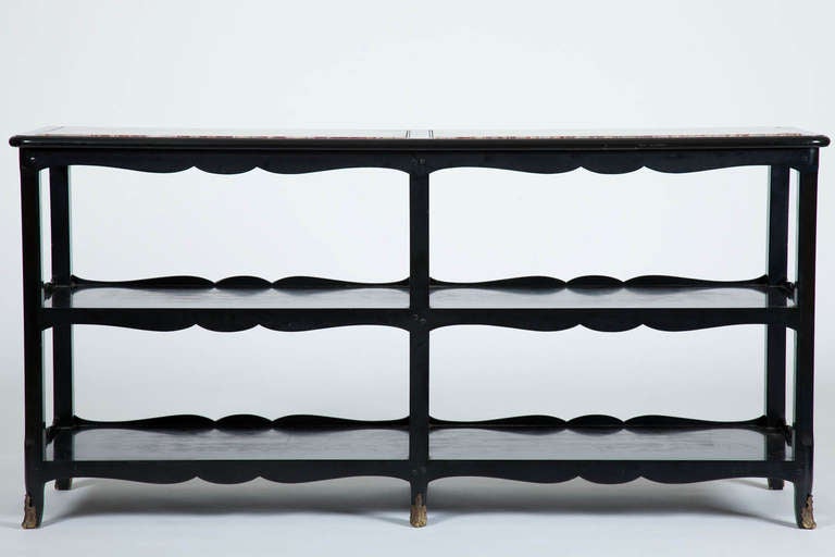 This mid twentieth century French long etagere has an ebonized wooden frame, the top with two inset pieces of marble, above two shelves, with curving aprons, supported by legs with gilded bronze cartouche form mounts, all in the Louis XV taste.