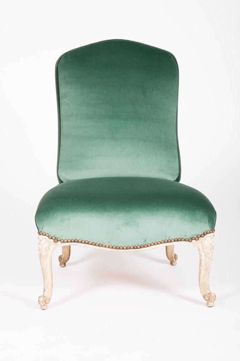 This slipper chair (chauffeuse) in the Louis XV taste was made by Maison Jansen's manufactory in Argentina. The shaped back, above a wide seat, is raised on grayish white painted carved cabriole legs. The underside upholstery retains the stamp