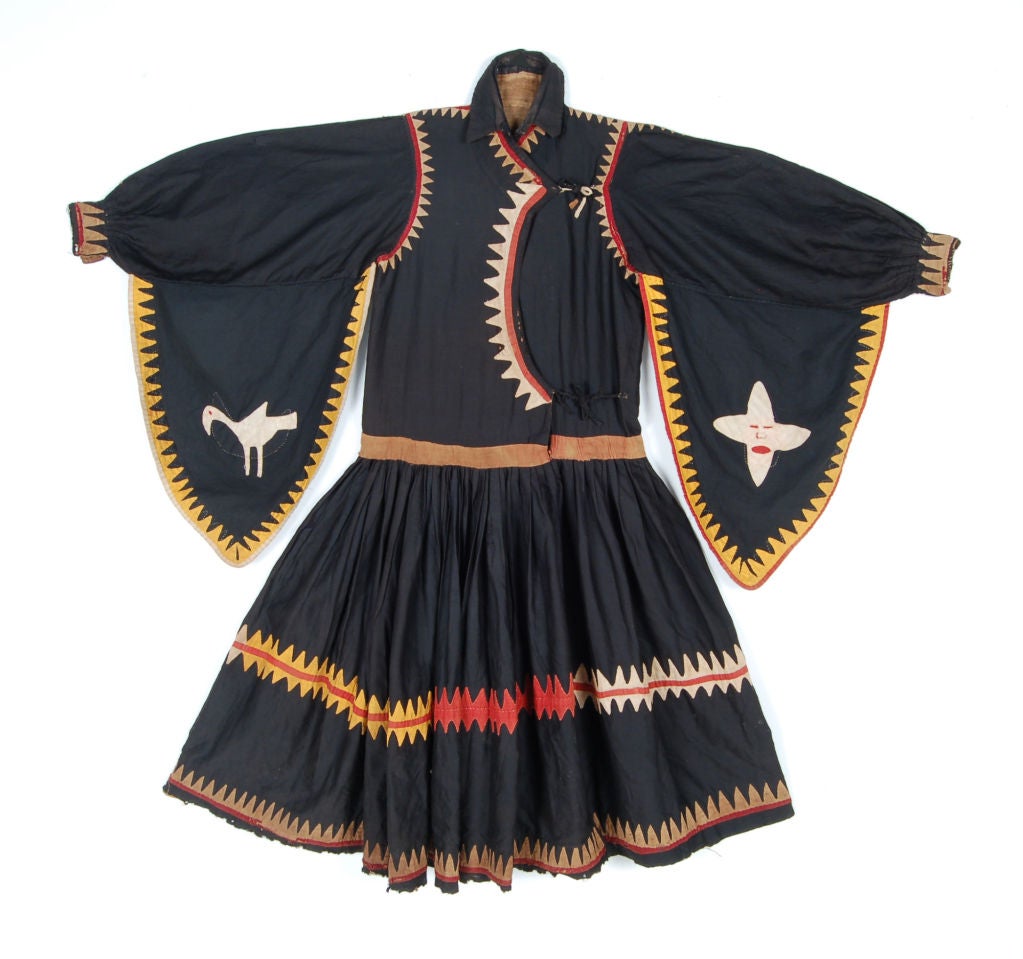 Man's dress with a long neck opening , pleated skirt and wide sleeves. Made of black tabby cotton and decorated with applique cotton of tan, red and orange cotton.