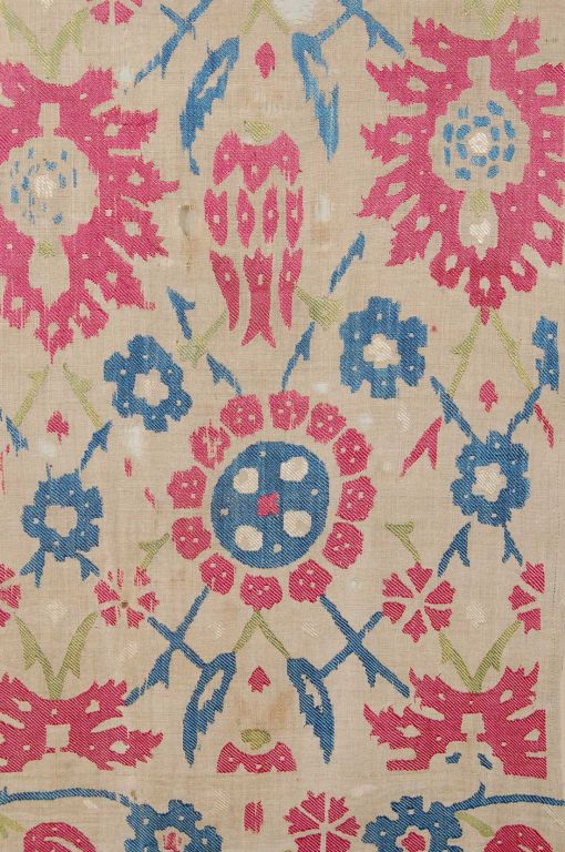 A large fragment of a linen coverlet embroidered with silk of three colors: Blue, red and green. A field of alternating rows of either tulips and large leaves or rosettes of two sizes. All shapes enclose within them some further petal ornamentation,