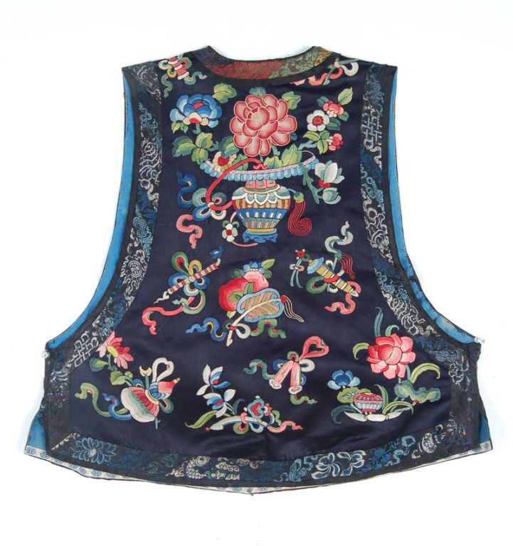 Non-official informal sleeveless coat of a Chinese woman. A waist length garment with front over flap closing to the right. It is fastened with five corded loops and toggle buttons and has a stand up collar and side vents. It is decorated in a