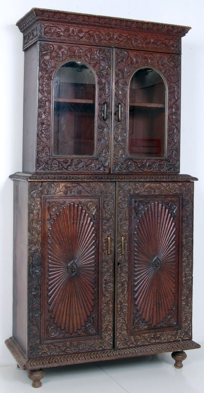 Two-part cabinet with extremely fine carving. The top part has a large cornice and two arched and glazed doors. The detailed carving around the glass has peacocks in the spandrels and meandering vines with large leaves and small berries. The bottom