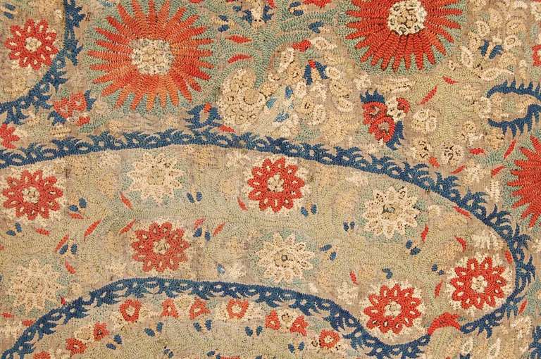 Embroidered linen fragment worked in silk in shades of blue, russet, green and ivory in herringbone stitch with crescent shaped leafy fronds containing round russet and ivory round flowers with more flowers filling up the rest of the field. The