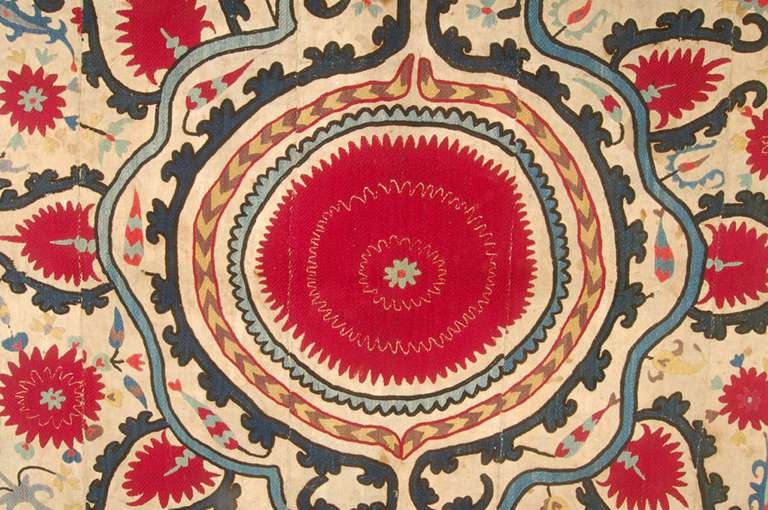 Unusual suzani with a center medallion of abstracted red flowers enclosed within four borders. The four corners feature triangular zoomorphic forms. Some more Botehs and flowers scattered in the field. The border plain and sparse.