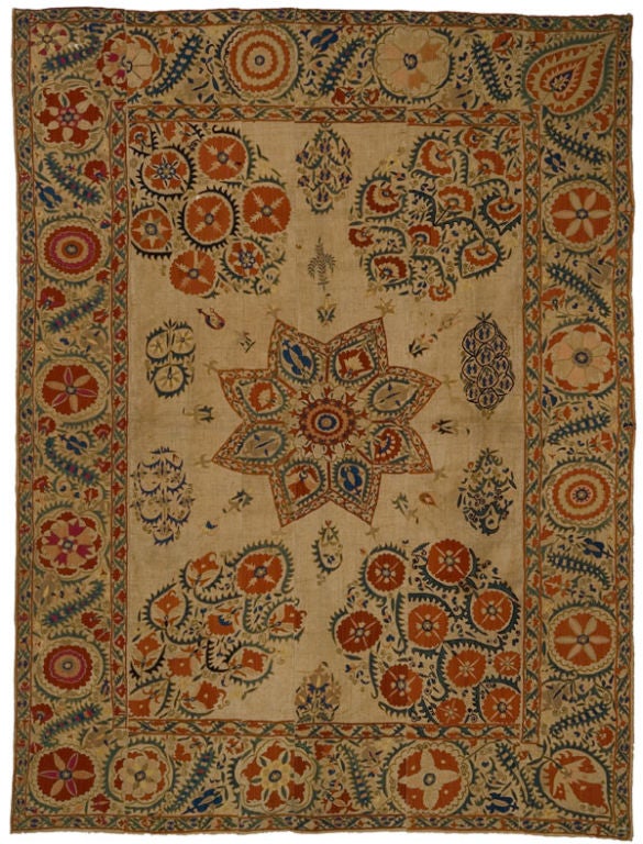 Large Suzani comprised of six panels, sewn together and embroidered in a floral shrub pattern. A large central star medallion and a large floral shrub in each corner dominate the center field, which also features other smaller shrubs and various