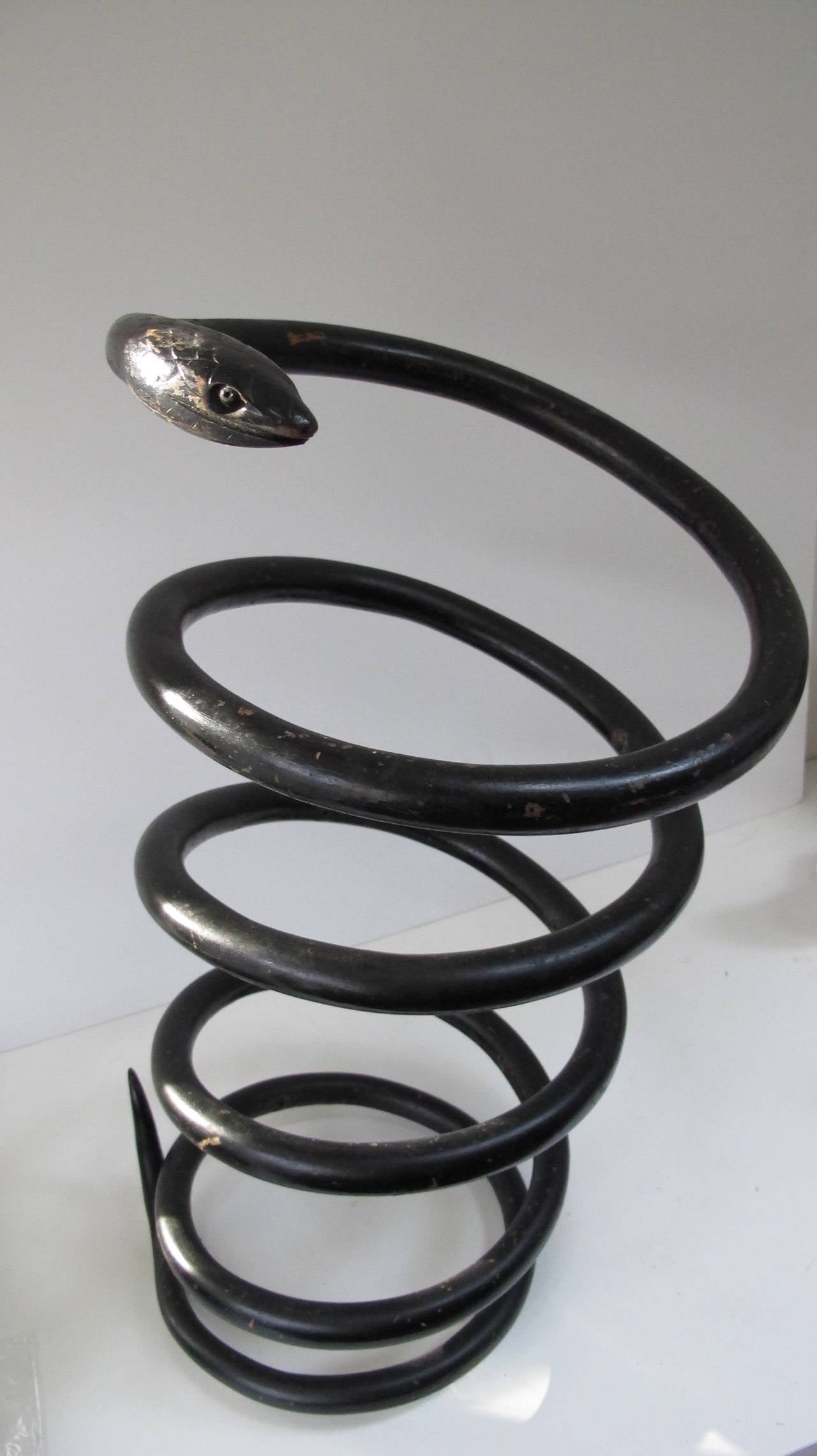 Spiral openwork snake in black paint. Rising in graceful arcs with a detailed carved head and lifted tail. I was told this was once made as a cane or umbrella Stand by an unknown maker. This piece has a wall mounting bracket that allows it to float