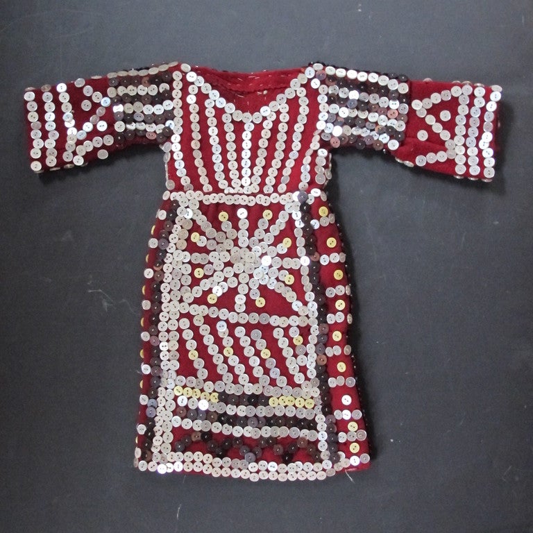 Pearly buttons sewn onto deep red trade cloth in various patterns.  Combinations of light and dark buttons used. I sold this years ago to a collector of Native American children's pieces. This relates to Nothwesst coast button blankets but it's