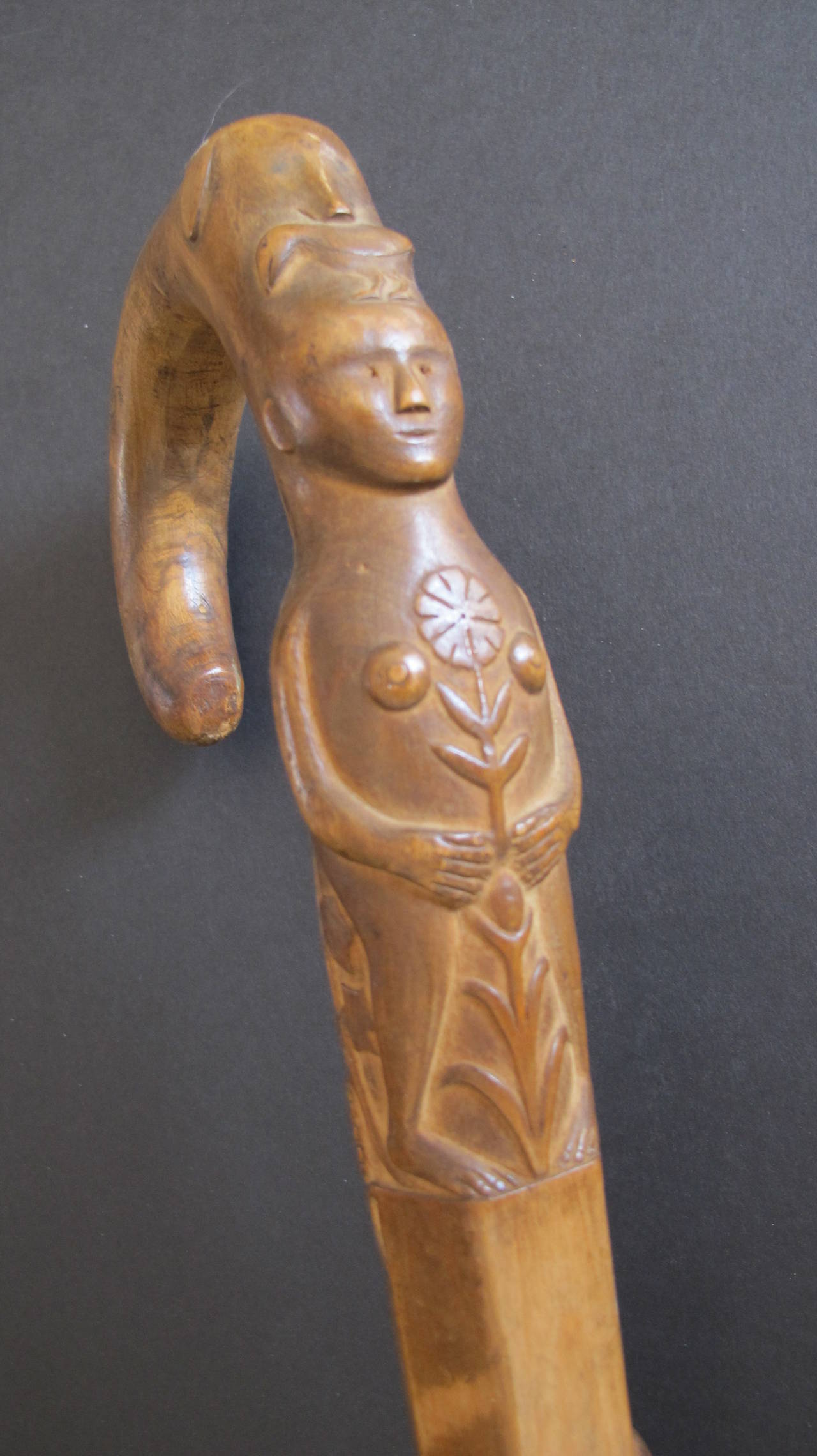 Exceptional carved Folk Art cane with a woman holding a flower with a dog and bird on top of the arched handle. The pot the figure is standing on has grape vines growing on the back and another dog surrounded by spiraling snakes.
The cane has an