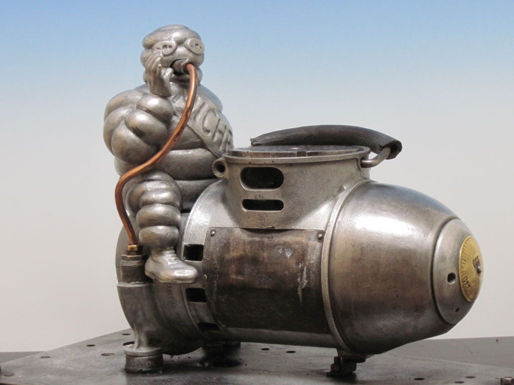 Vintage aluminum Michelin Man astride the compressor made to fill tires.  Appearing like the man in Dr. Strangelove falling to earth on the bomb.  Michelin man has a copper tube from the mouth and rests on its original mounting base. Handy carry