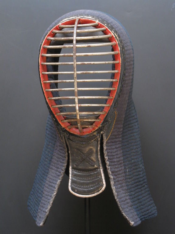 Kendo, the Japanese martial art. The mask is of finely crafted graphic steel, leather and quilted cotton with red lacquer edging to enhance the ferocity of the face. Mounted on metal base