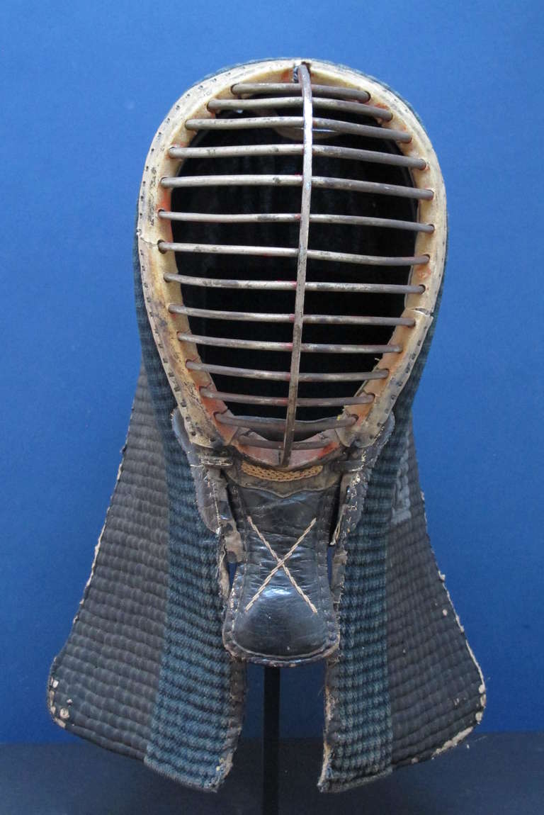 Finely crafted Japanese Kendo mask for martial arts using a fighting stick.  Padded cloth with leather and iron face protection.  A remarkable design object with the curved iron face protection, patterned padding and written markings on the side.