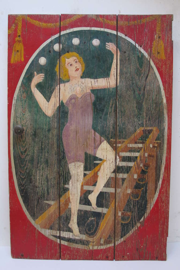 The sideshow painting of a woman juggling 4 balls while standing on a swords ladder.The painting on wood panel was the door on the barkers podium and retains the wood knob on the left side and would have had hinges on the tight edge. This would have