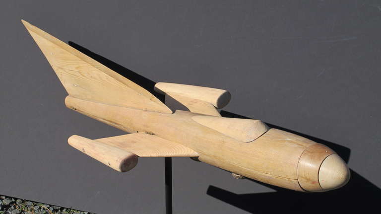 Finely made wooden airplane model made as a prototype with hinged body that opens to reveal detailed engine. The plane has a large tail fin and small swept back wings with end pods. The nose cone is made of 2 turned pieces of wood and turns freely.