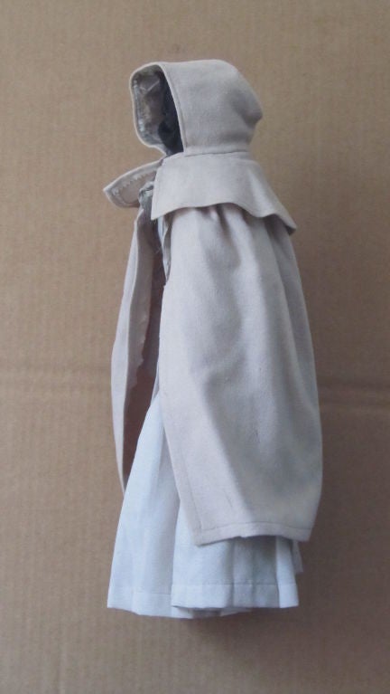 Finely made doll's hooded wool cloak and dress made by a Shaker seamstress. The invisible Shaker doll floating ethereally in space from a minimal wall bracket. Ohio.