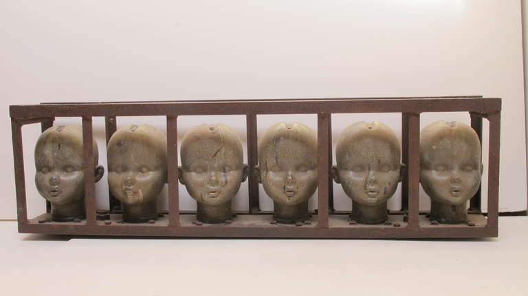 Finely molded series of 6 large doll heads molds in industrial iron cage. The head forms are made of copper and have a well preserved patina. As doll manufacturing went East the doll factories closed in this country revealing a different kind of
