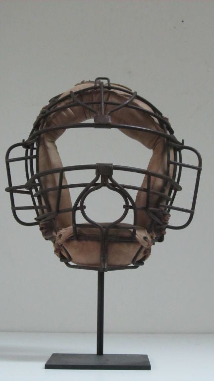Graphic catchers mask with circular mouth opening suitable for spitting. This type of baseball can be seen in early baseball photos from the 1930-40s. Mounted on back metal AP base
