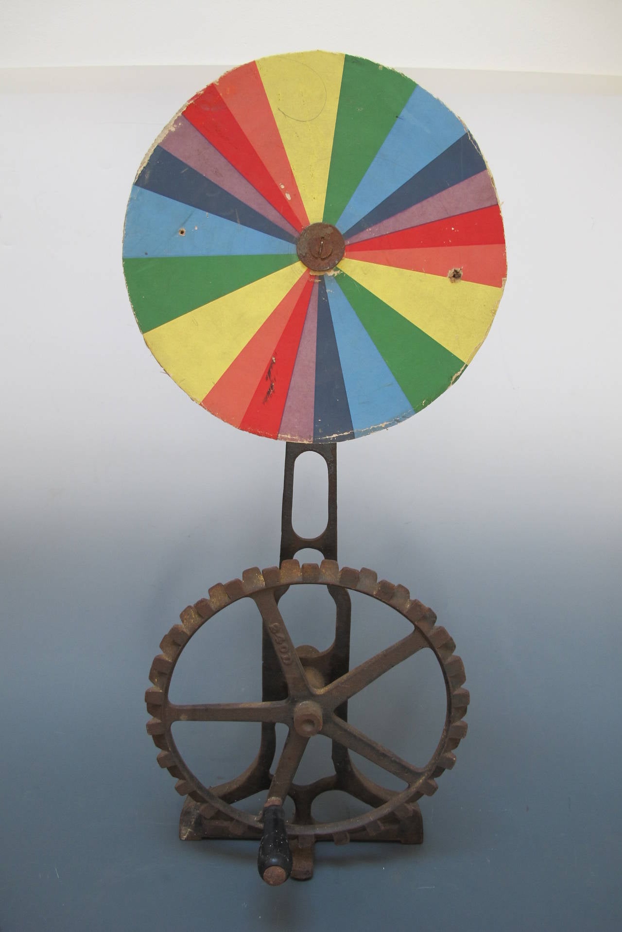 A rare and mysterious color wheel of interesting proportions fixed to a perforated metal disc backing attached to a cast iron base structure. On the lower part is a gear form with wooden hand crank. Oddly the upper and lower wheels are not