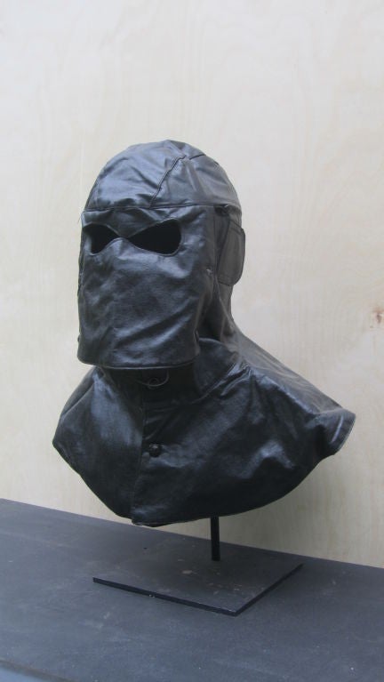 Pieced leather helmet was worn to protect against cold in the depths of the sea for the submarine torpedo man. Black leather mask with eye openings and broad shoulder covering.  Evoking the dark side of Darth Vader. labeled inside 1957. Mounted on