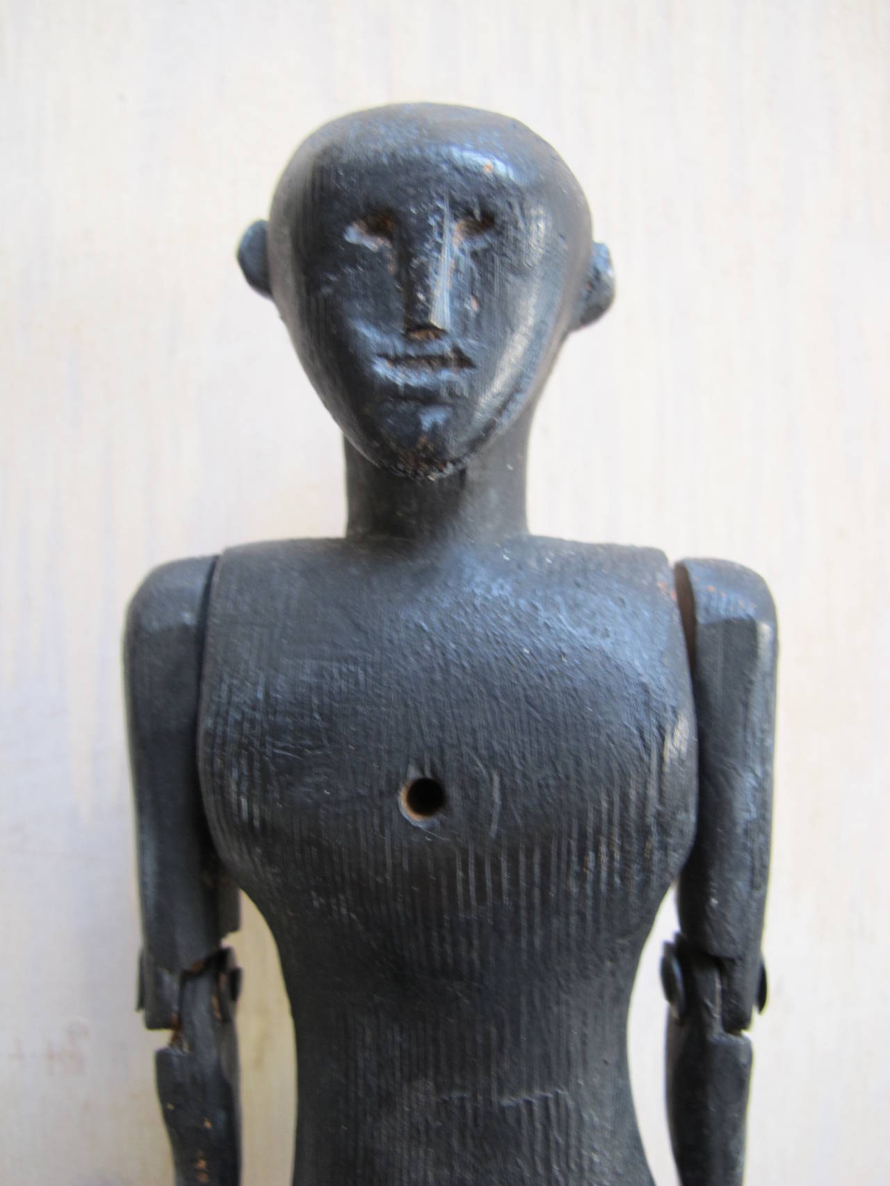 An early American dancing toy figure of carved and painted wood. The carved face has a strong face with simplified features. The arms and legs can move freely and the chest has a hole through it so that a stick or stiff wire can be inserted from the