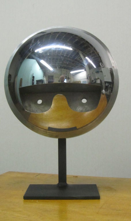 Nickel plated iron half sphere with deeply recessed eye glasses negative form.  The polished reflector form distorts everything around it in the manner of an Anish Kapoor sculpture.  Mounted over black metal base. In the first image what appears to