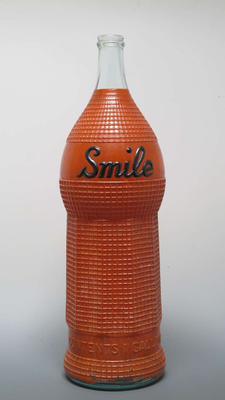 The Orange Smile Syrup Company used to be one of the leading suppliers of soda fountain syrups. This bottle was a trade stimulator for the soda fountain to advertise its flavored syrups on or behind the counter. The painted glass bottle is shapely