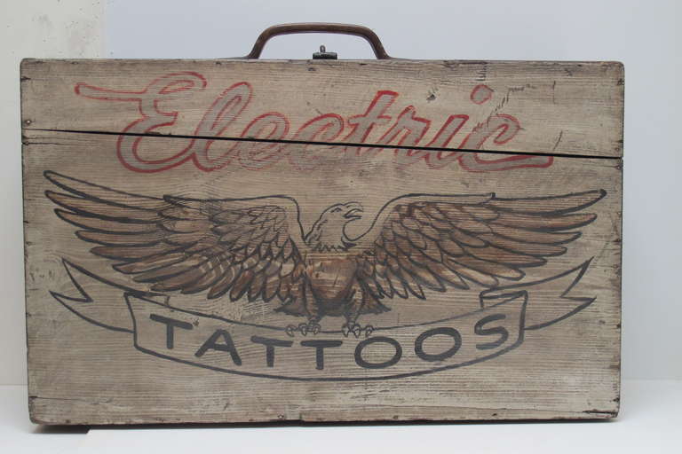 Well made hinged wood travel case with wood handle made to hold a tattooist's equipment and possibly flash samples. Painted on the front of the case is Electric Tattoo with a well drawn spread winged eagle.I am guessing mid century as the Electric