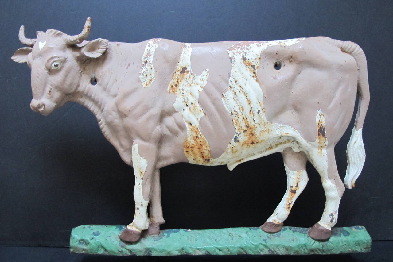 Finely modeled iron cow made to indicate a dairy farm. Modeled in relief the painted cow would have been screwed onto a sign or building. Found in upstate New York. Mounted over a black metal table stand.