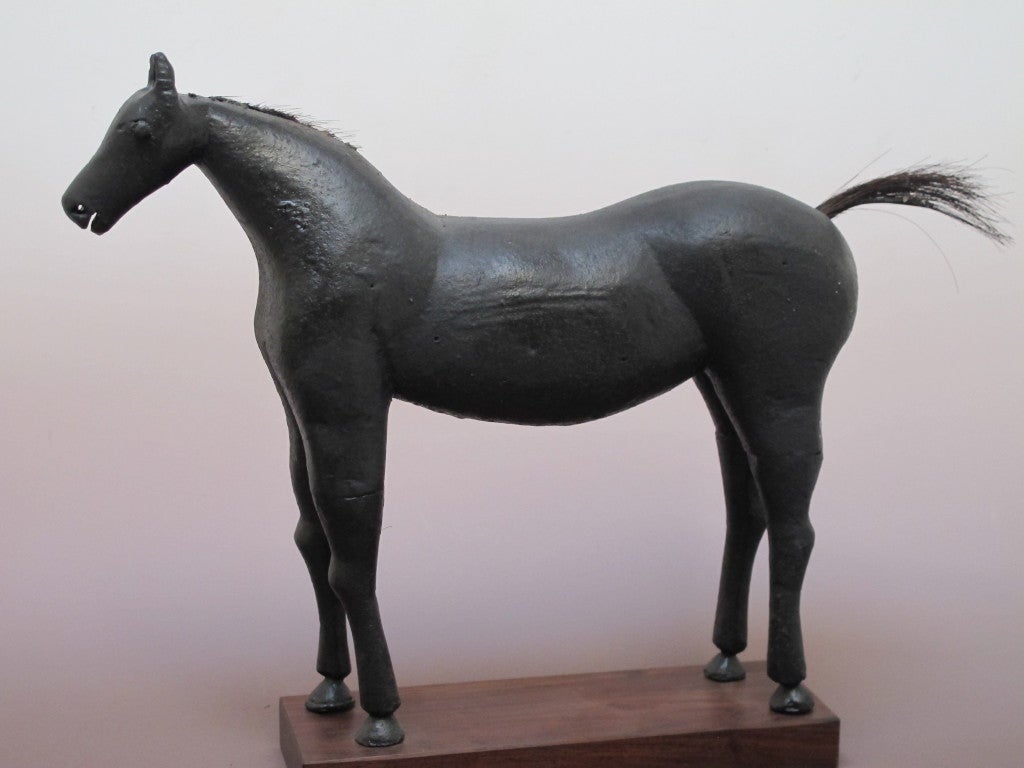 This folk sculpture has a wood body with attached carved legs. Black painted surface and a horsehair tail. Mounted on wood base.